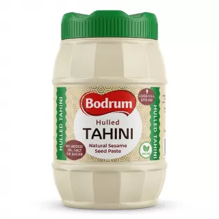 A front-facing studio shot of Bodrum Hulled Tahini in a 900g ribbed plastic jar with a green cap, featuring a clean white label. The jar is centered against a seamless white background with a soft shadow at its base.