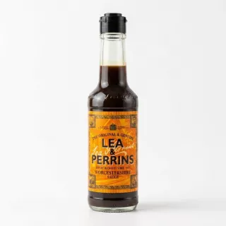 A 150ml glass bottle of Lea & Perrins Worcestershire Sauce, featuring its distinctive orange and yellow label, is held in a person's hand against a clean white studio background. The bottle is well-lit with soft shadows, highlighting the dark, matured sauce inside. PRODUCT TITLE: Lea & Perrins Worcestershire Sauce - Authentic Matured 150ml