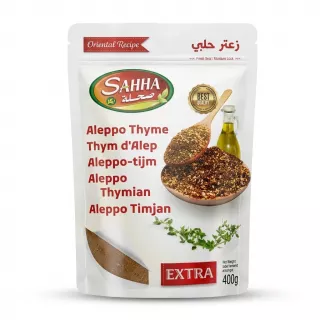A 1:1 professional product photo of a 400g Sahha Aleppo Thyme Extra blend resealable stand-up pouch, centered on a seamless white background with even studio lighting and a soft, symmetrical contact shadow. The white pouch, filling 85% of the frame, features the 'SAHHA' brand logo and product information in multiple languages (English, French, Dutch, German, Swedish) and Arabic text. The product graphic shows two wooden spoons holding the za'atar spice mix and a bottle of olive oil, with fresh thyme sprigs. All text is crisp and clear, and the pouch is in pristine condition without any store tags or imperfections.