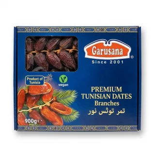 A 900g box of Garusana Premium Tunisian Dates, featuring whole dates on branches visible through a clear window, is centered on a white background with a subtle shadow. The blue box has golden borders, the brand name, and details about its origin in Tunisia and vegan status.