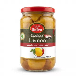 A 720g glass jar of Sofra Pickled Lemon Egyptian Style with a red lid, featuring a green label with English and Arabic text and an illustration of lemons and a red chili. The jar is centered on a clean white background. PRODUCT TITLE: Sofra Pickled Lemon Egyptian Style PRODUCT: A professional, studio-quality e-commerce photograph of a 720g glass jar of Sofra Pickled Lemon Egyptian Style, as seen in image_0.png. The jar is centered and fills approximately 85% of the frame. All background elements (hand, store shelves, etc.) have been completely removed. The jar stands on a pristine, seamless white surface. The product label is meticulously cleaned, retaining all factual information: the 'Sofra' logo, 'Pickled Lemon' text, the red 'Egypt Style' band, the full Arabic text "ليمون مخلل حار بالعصفر" and "النكهة المصرية", the image of the lemons and red chili, and the '720g e' weight. Crucially, the yellow and red price sticker ('£1.69' and arrow) and the small green 'Hot' sticker have been seamlessly removed, revealing the clean, continuous label paper and text behind them. The jar is lit with soft, diffused professional studio lighting that is even across the entire product, with no harsh highlights or uneven shadows. Soft, equal-intensity shadows are cast on both the left and right sides of the base of the jar, giving it a stable presence. The glass texture is rendered clearly, showing the liquid brine and whole pickled lemons inside. The focus is tack-sharp on the central label and the front of the jar. The aspect ratio is 1:1 square.