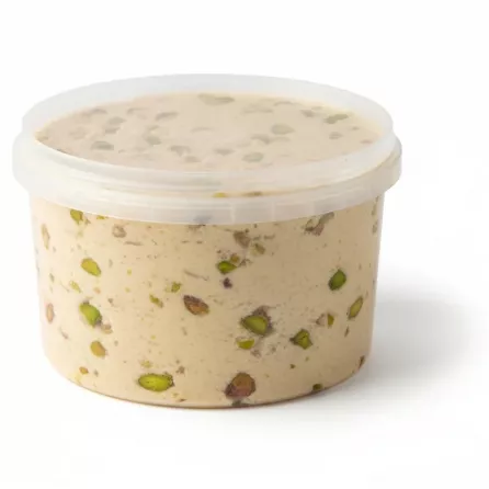 Side view showing pistachio pieces embedded in halawa inside transparent plastic tub