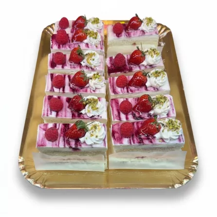 Selection of bright berry delight cake slices topped with strawberries, raspberries, whipped cream and crushed pistachios on a golden tray