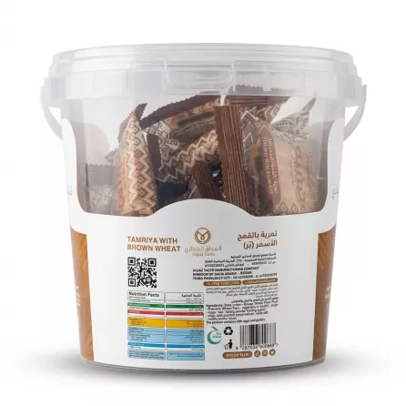 A clear plastic tub of Hijazi Taste Tamriya with Brown Wheat, filled with individually wrapped pastries, featuring a detailed label with nutritional information in English and Arabic on a pure white background. PRODUCT TITLE: Hijazi Taste Tamriya Brown Wheat