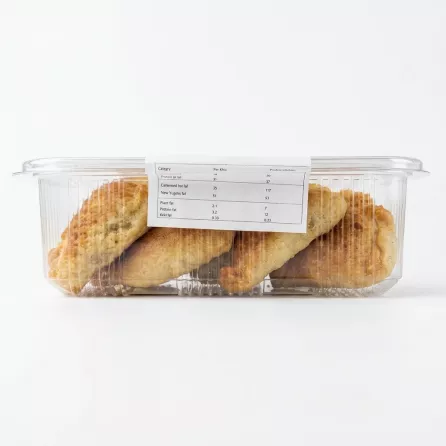 A clear plastic container of baked pastries, as seen in a side view. The label, with all its original text and data, is cleanly displayed and perfectly legible, centered on the front of the packaging. The four maamoul cookies are clearly visible through the plastic against a pure white background with soft, even studio lighting.