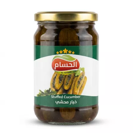 A professional front view studio shot of a glass jar of Al Hussam Stuffed Cucumber with a green and white label and a gold lid, centered on a plain white background with soft shadows.