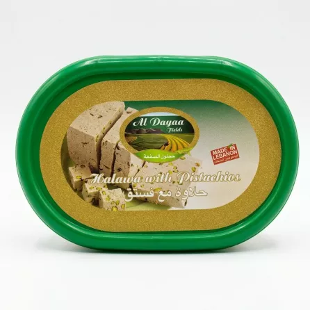 A 1:1 professional e-commerce product photograph features a centered green plastic tub of Al Dayaa Halawa with Pistachios. The shimmering gold and white label displays the product brand, title in English and Arabic, and a "MADE IN LEBANON" stamp. All background elements, imperfections, and external tags have been removed. The product fills 85% of the frame, is in sharp focus, and is illuminated by professional studio lighting with a soft, even shadow.