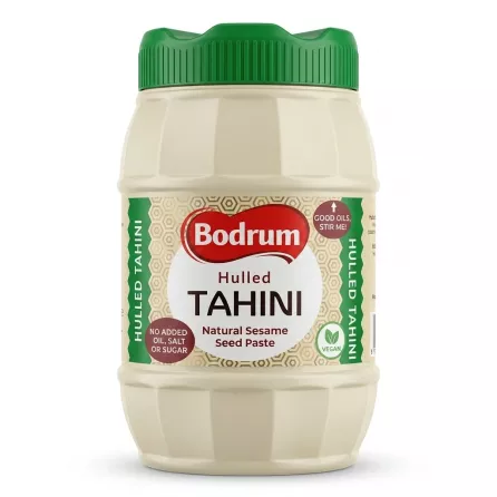 A front-facing studio shot of Bodrum Hulled Tahini in a 900g ribbed plastic jar with a green cap, featuring a clean white label. The jar is centered against a seamless white background with a soft shadow at its base.