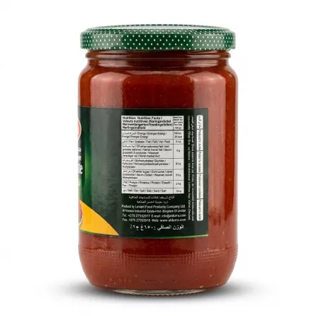 A 1:1 professional e-commerce product photograph of the back of a 650g glass jar of Durra Pepper Paste. The product is isolated on a pure white background with even soft shadows on both sides. The sharp focus clearly displays the detailed nutrition facts, ingredients, and producer information in English and Arabic. The green lid with white dots and the red color and texture of the paste are clearly visible, with all supermarket background elements and the hand removed.