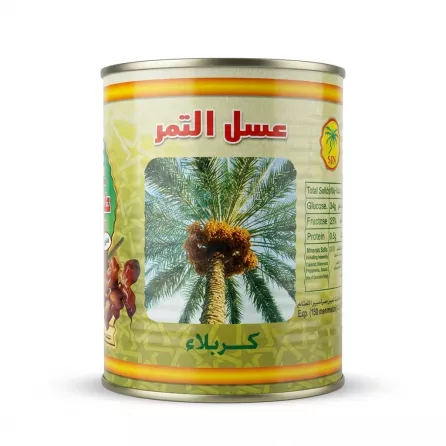 A professional e-commerce product photograph of a tin of SJN Date Syrup from Karbala. The yellow and green tin, centered on a pure white background, prominently features an illustration of a date palm tree with fruit. Above the tree, the Arabic text "عسل التمر" (Date Syrup) is in red, and below the tree, "كربلاء" (Karbala) is in green. A factual nutritional information panel is clearly visible on the right.
