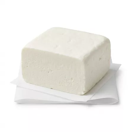 ** A studio photograph of a centered, white block of Milky's Reduced Fat White Sour Cheese with a smooth, compact texture, presented on a white folded paper wrap.