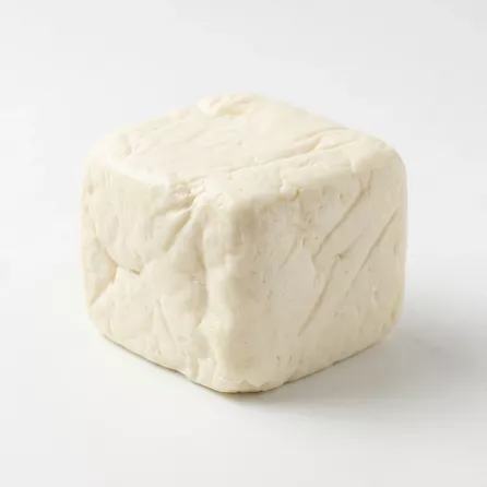 A professional studio photo of a square block of white, unwrapped Halloumi cheese. The cheese block, with its natural texture and shape, is presented on a clean white surface with a soft, even shadow, showing the product in clear detail.