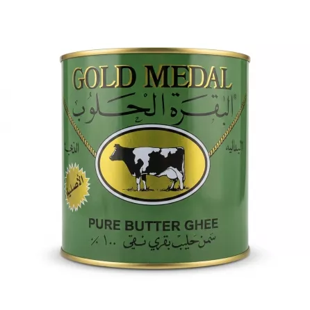 A 1:1 professional e-commerce studio photograph of a 1600g tin of Gold Medal Pure Butter Ghee on a pure white background. The green tin is centered and fills 85% of the frame. It features a sharp, clean label with a black and white cow in a gold oval, the text 'GOLD MEDAL', 'البقرة الحلوب', 'PURE BUTTER GHEE', and 'سمن حليب بقري نقي' clearly legible. All tags, labels, and imperfections have been removed. The tin is perfectly level with a soft, symmetrical contact shadow.