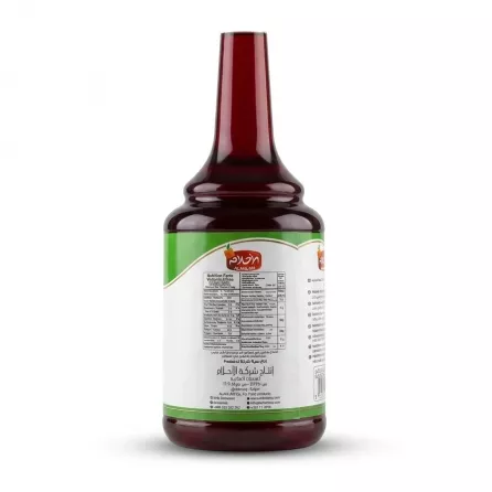 A 1:1 square-format studio photograph showing the back view of an AlAhlam Pomegranate Concentrate Syrup bottle, centered on a clean white background. The large white paper label displays the "AlAhlam" logo, a clear nutrition facts table, and ingredients list in multiple languages, with professional lighting ensuring high legibility and a sharp focus on all factual details.