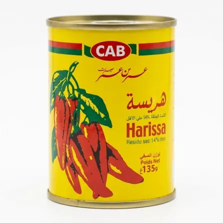Hand holding a 135g tin of CAB Harissa Paste with red chillies on yellow label