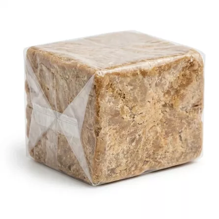 Hand holding a block of natural African black soap wrapped in clear plastic