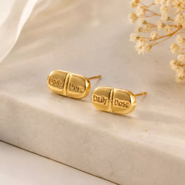 14K gold plated Daily Dosage Pill Stud Earrings displayed on a minimalist marble surface, showcasing the polished capsule design engraved with "Daily Dose".