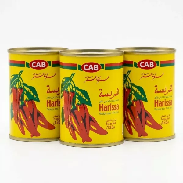 Hand holding a 135g tin of CAB Harissa Paste with red chillies on yellow label