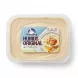 A top-down view of a clear plastic tub filled with hummus and sealed with clear film. A central rectangular label displays 'Dairy Day HUMUS ORIGINAL' text with Arabic and icons, a bowl of hummus image, and '200g e', while a price tag has been removed.