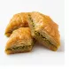 A close-up studio photograph of three pieces of diamond-shaped Sultan pistachio baklava on a solid white background, showcasing the flaky pastry layers and green nut filling.